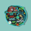 Embroidered patch with a teal border showing two illustrated girls, one aiming a bow and arrow and the other holding the Earth, surrounded by stars, leaves, and flowers with stitched motivational text