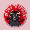 Round embroidered patch with a smiling cartoon bull on a red background, surrounded by the words “Be True to Yourself” and small floral details.