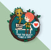 “Embroidered circular patch featuring a smiling plant figure in a pot seated next to a child in a scout-style outfit on a bench, framed by vines and leaves, with a heart symbol and environmental message stitched at the bottom.”