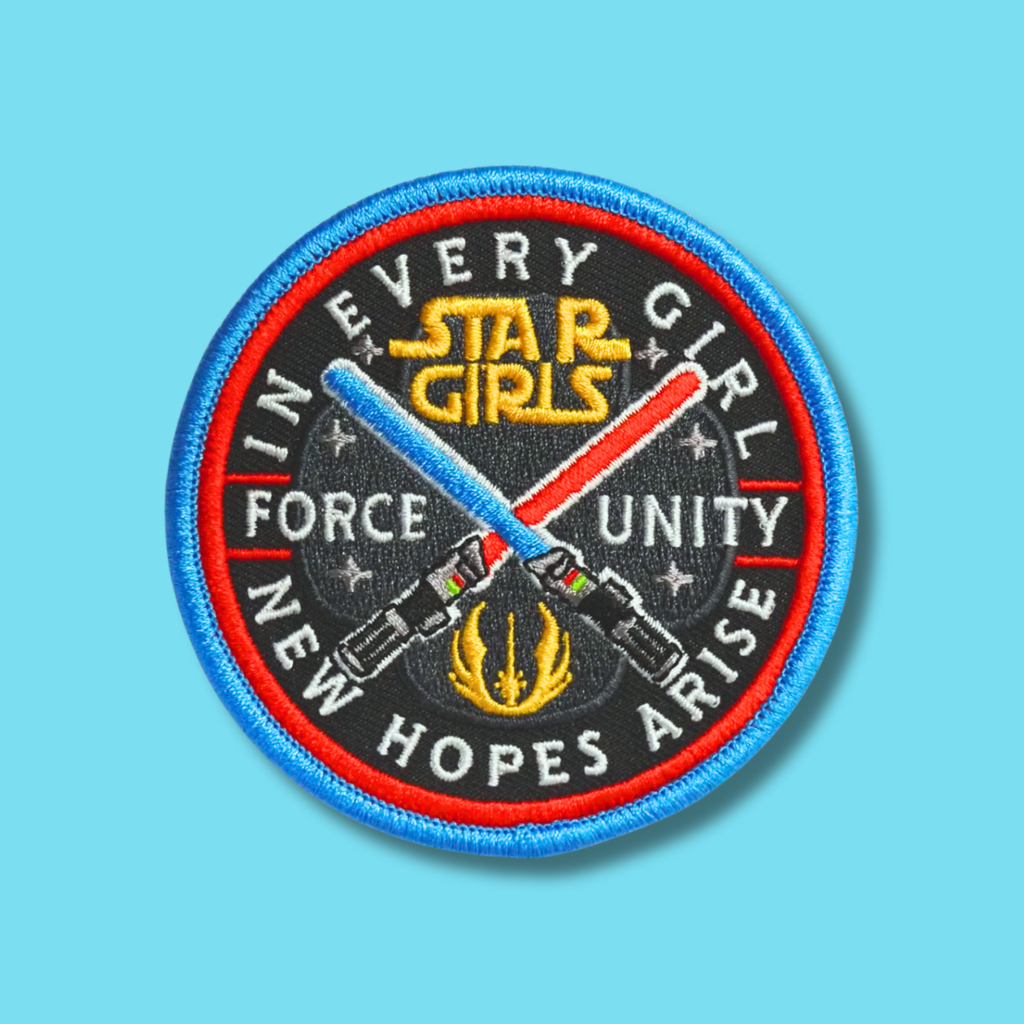 Embroidered circular patch with the phrase ‘In Every Girl, New Hopes Arise’ and crossed light-themed swords.