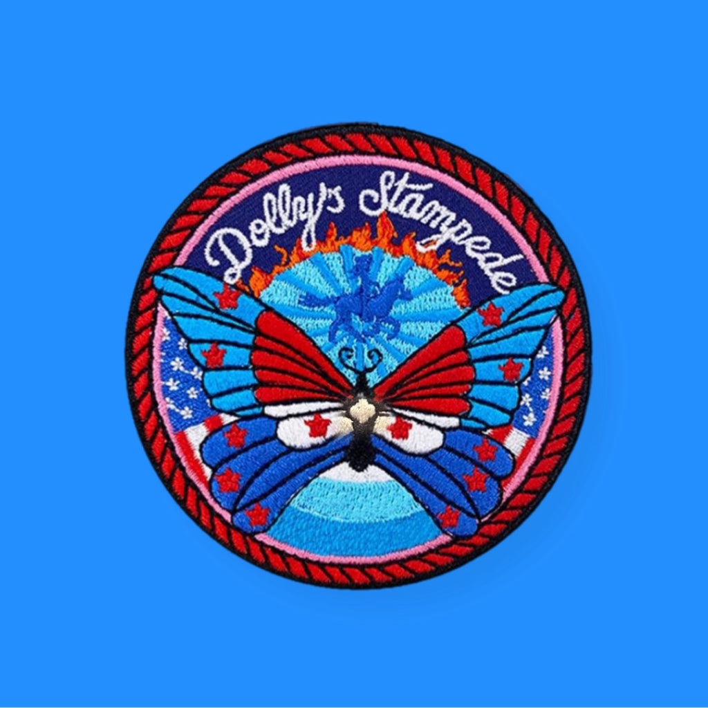 Round embroidered patch featuring a colorful butterfly with red, blue, and white wings, surrounded by stars and a decorative border, set against a blue background with radiant patterns.