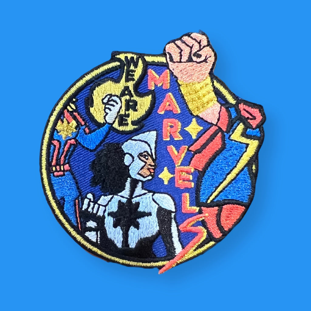 “Round embroidered patch showing a powerful illustrated figure with a raised fist, lightning bolts, and bold graphic shapes in blue, yellow, and red.”